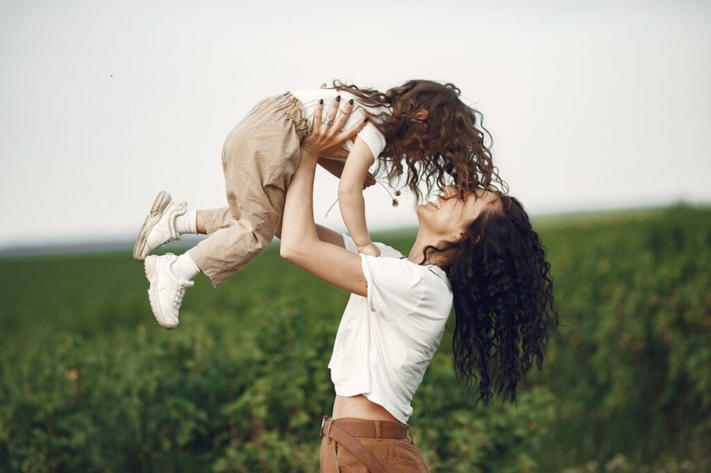 services-01 A mother lifts her daughter playfully in a sunny field, capturing a moment of joy and bond.